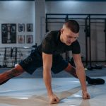 A male athlete stretches intensely in a dimly lit gym environment, preparing for training.