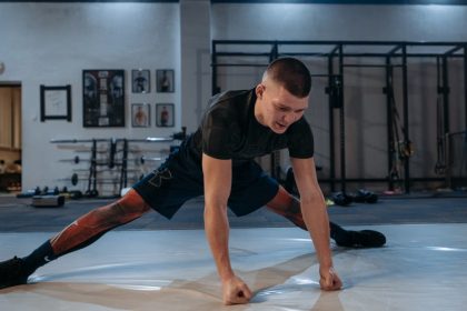 A male athlete stretches intensely in a dimly lit gym environment, preparing for training.