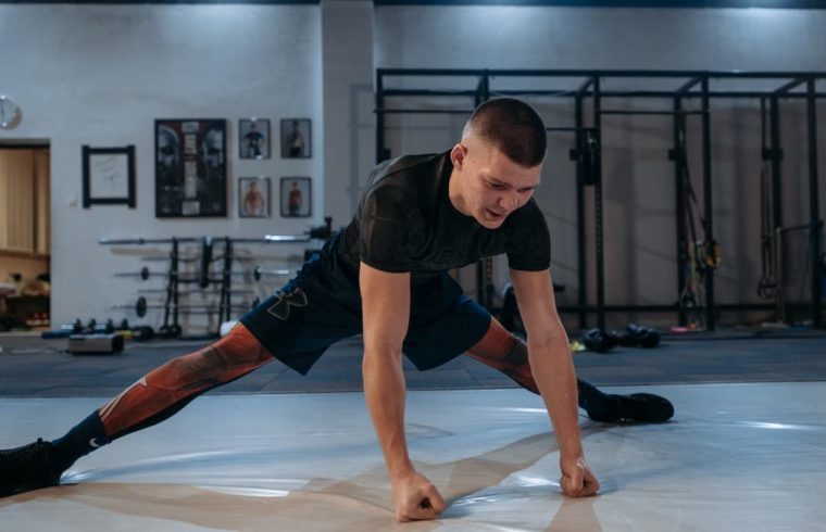A male athlete stretches intensely in a dimly lit gym environment, preparing for training.